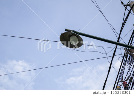 Streetlight against blue sky and tangled wires providing illumination in urban area, natural light with ample copy space for text overlay Streetlight against blue sky and tangled wires providing illumination in urban area, natural light with ample copy space for text overlay 135258301