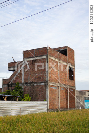 Unfinished brick building under construction with natural light, surrounded by green field and clear sky, providing copy space for real estate development projects Unfinished brick building under construction with natural light, surrounded by green field and clear sky, providing copy space for real estate development projects 135258302