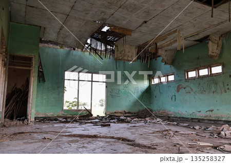 Dilapidated building interior with natural light shining through the window and damaged roof, creating a sense of abandonment and decay Dilapidated building interior with natural light shining through the window and damaged roof, creating a sense of abandonment and decay 135258327