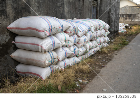 Stacked sacks leaning against weathered wall with copy space, showcasing storage and logistics challenges in rural environment Stacked sacks leaning against weathered wall with copy space, showcasing storage and logistics challenges in rural environment 135258339