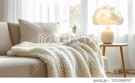 Cozy Minimal Living Room with Knitted Wool Blanket on Sofa, White Window and Sheer Curtains, Decorated with Cloud Lamp Cozy Minimal Living Room with Knitted Wool Blanket on Sofa, White Window and Sheer Curtains, Decorated with Cloud Lamp 135260057