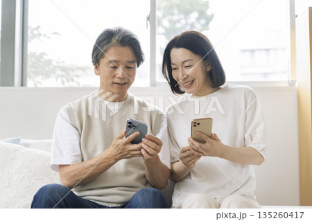 スマートフォンの画面を見る笑顔の50代の夫婦 スマートフォンの画面を見る笑顔の50代の夫婦 135260417