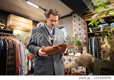 Serious handsome man customer thinking on buying fancy leather shoes in second hand vintage shop. 135260956