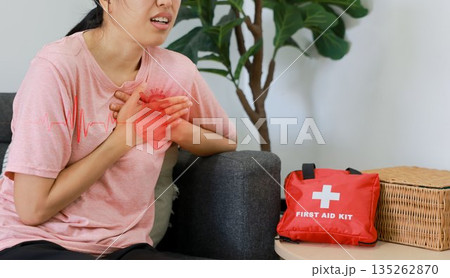 Asian woman sitting on sofa clutching chest with heart pain concept, healthcare, cardiology, emergency symptom, stress, medicine and heart attack awareness with ECG graphic overlay. Asian woman sitting on sofa clutching chest with heart pain concept, healthcare, cardiology, emergency symptom, stress, medicine and heart attack awareness with ECG graphic overlay. 135262870