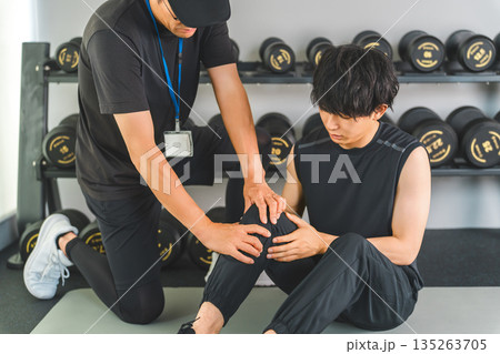 膝関節を痛がるトレーニングをする男性とスポーツ理学療法士の男性スタッフ 膝関節を痛がるトレーニングをする男性とスポーツ理学療法士の男性スタッフ 135263705