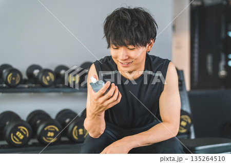 ジムでトレーニング後にゼリー飲料で栄養補給する若いアジア人男性 ジムでトレーニング後にゼリー飲料で栄養補給する若いアジア人男性 135264510