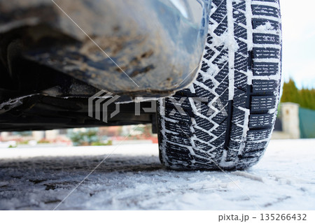 Winter car tire with snow on tread on icy road 135266432