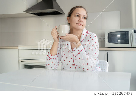 Woman in heart-patterned pajamas drinking coffee in her kitchen, enjoying a moment of solitude and reflection 135267473