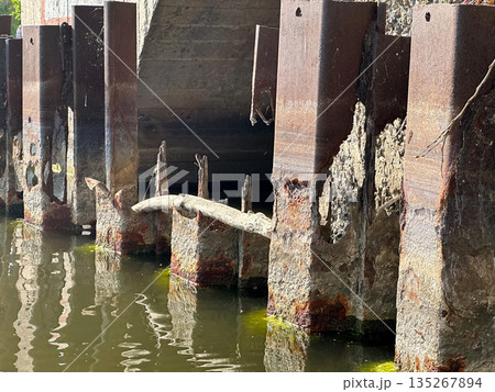 Rusty metal pillars in water showing decay and erosion effects. 135267894