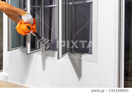 Handyman using a blower for cleaning  exterior window frame. 135269665