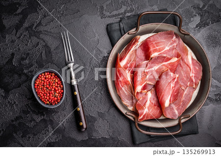 Thin slices of Speck, Jambon Italian cured meat. black background. top view Thin slices of Speck, Jambon Italian cured meat. black background. top view 135269913