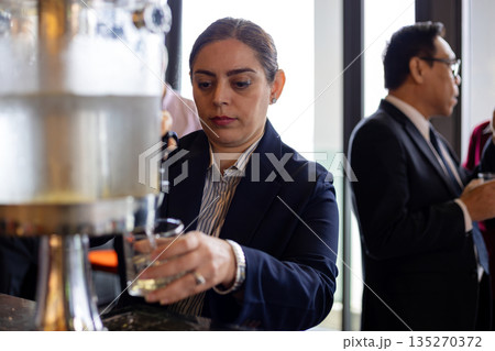 professional woman in business attire pouring a drink from a dispenser at a corporate networking event, highlighting professionalism and event hospitality professional woman in business attire pouring a drink from a dispenser at a corporate networking event, highlighting professionalism and event hospitality 135270372