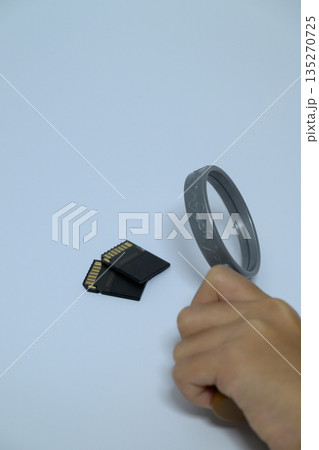 虫眼鏡でSDカードを調べる手元の縦位置写真 虫眼鏡でSDカードを調べる手元の縦位置写真 135270725