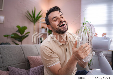 Man refreshing himself with a fan during a heat wave at home Man refreshing himself with a fan during a heat wave at home 135273094