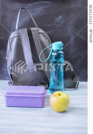 Backpack, lunch box, apple and water bottle on table near school blackboard, back to school concept Backpack, lunch box, apple and water bottle on table near school blackboard, back to school concept 135273436