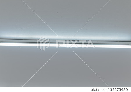 Fluorescent light fixture emitting bright light on a white ceiling with copy space offering minimalist interior design applications Fluorescent light fixture emitting bright light on a white ceiling with copy space offering minimalist interior design applications 135273480