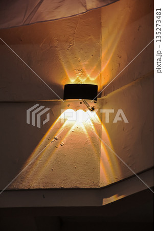 Modern wall lamp emitting rays of warm light on textured wall, creating dramatic shadows for home decor and architectural design with ample copy space Modern wall lamp emitting rays of warm light on textured wall, creating dramatic shadows for home decor and architectural design with ample copy space 135273481