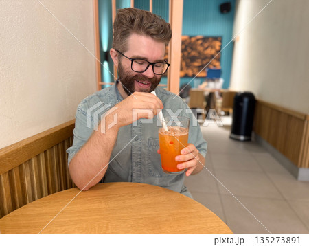 Man enjoying iced fruit tea at wooden cafe table. Relaxed mood, everyday routine, and casual refreshment through modern beverage lifestyle Man enjoying iced fruit tea at wooden cafe table. Relaxed mood, everyday routine, and casual refreshment through modern beverage lifestyle 135273891