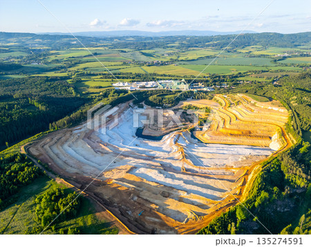 The sandstone quarry in Strelec shows multiple layers of excavated earth and rock. The surrounding fields and hills are visible in the distance under a clear sky. 135274591