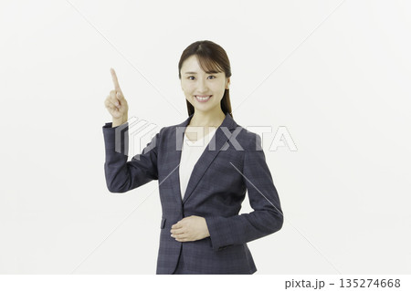 白背景の指さしポーズをするカメラ目線のスーツを着た若い日本人女性のポートレート 135274668