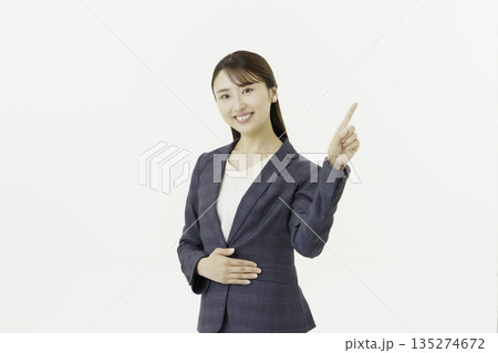 白背景の指さしポーズをするカメラ目線のスーツを着た若い日本人女性のポートレート 135274672