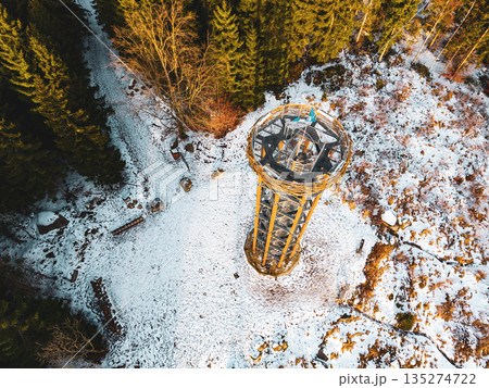 Visitors stand at the top of Svetly vrch lookout tower in Albrechtice. The ground is covered with snow, and the surrounding trees are bare. The scene captures winter in the mountains. 135274722