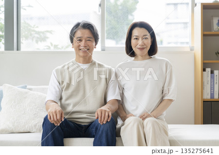 ソファに並んで座るカメラ目線で笑顔の50代の夫婦 ソファに並んで座るカメラ目線で笑顔の50代の夫婦 135275641