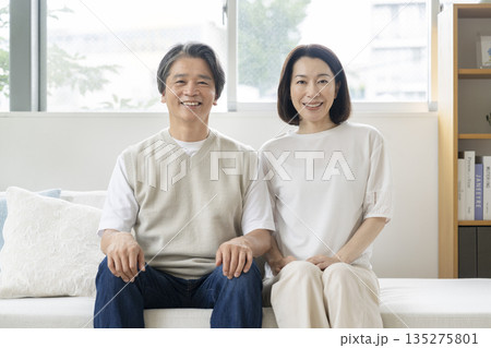 ソファに並んで座るカメラ目線で笑顔の50代の夫婦 イメージ ソファに並んで座るカメラ目線で笑顔の50代の夫婦 イメージ 135275801