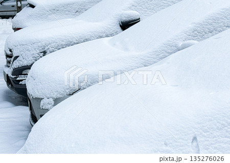 Rows of vehicles sit completely submerged under heavy accumulation of fresh snow. Winter driving hazards, car maintenance in winter, snow-covered vehicles, road safety. Rows of vehicles sit completely submerged under heavy accumulation of fresh snow. Winter driving hazards, car maintenance in winter, snow-covered vehicles, road safety. 135276026