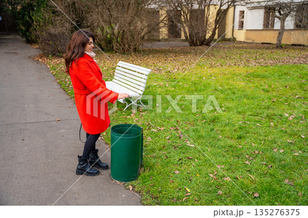 Woman throwing trash into outdoor park bin while walking in Prague during winter. Responsible everyday behavior, urban lifestyle routine and care for public space in real life city environment Woman throwing trash into outdoor park bin while walking in Prague during winter. Responsible everyday behavior, urban lifestyle routine and care for public space in real life city environment 135276375