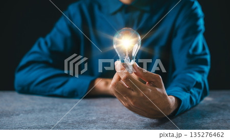 Hand holds glowing bulb light moment for idea, innovation, lightbulb, business background concept, power, digital inspiration flows through creative mind while person sits at desk 135276462