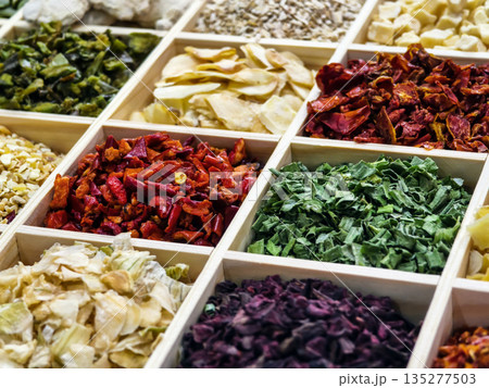 Vibrant display of dried spices and herbs in wooden boxes at a market stall in a busy town square Vibrant display of dried spices and herbs in wooden boxes at a market stall in a busy town square 135277503