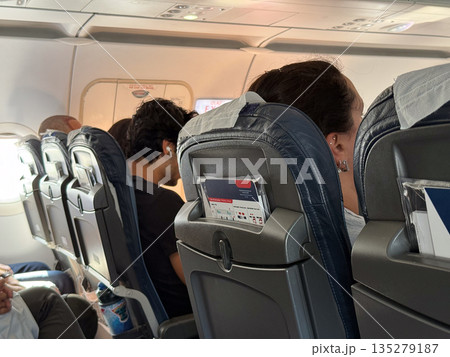 Passengers seated in airplane cabin during flight. Inflight comfort, travel experience, and modern transportation through aircraft interior 135279187
