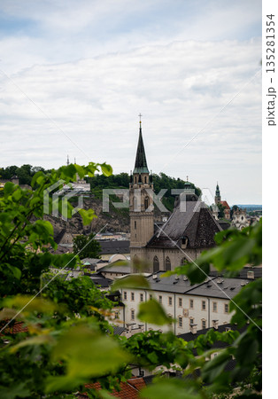 Scenic view of historic Salzburg old town with church spire framed by green leaves 135281354