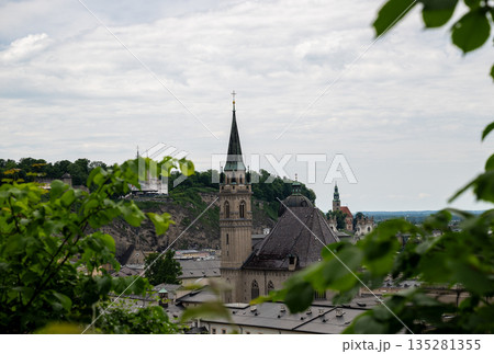 Scenic view of historic Salzburg old town with church spire framed by green leaves 135281355