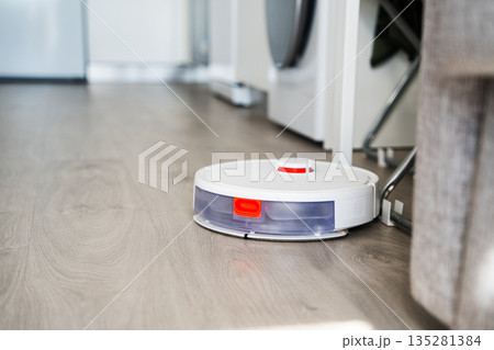 Smart robot vacuum cleaner navigating living space near furniture, automatic floor cleaning in modern minimalist home interior Smart robot vacuum cleaner navigating living space near furniture, automatic floor cleaning in modern minimalist home interior 135281384