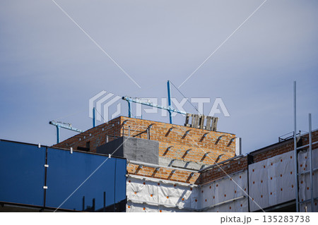 Workers are constructing a new building with brick walls and metal supports visible at the top. The sky is clear as the project moves forward in the city 135283738