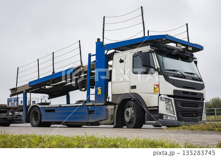 A heavy truck stands at a loading area. Ramps are visible on top, ready for loading vehicles. The sky is cloudy, and the environment is industrial 135283745