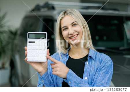 Saleswoman showing calculator and explaining car cost in dealership Saleswoman showing calculator and explaining car cost in dealership 135283977