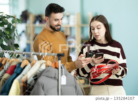 Woman selects handbag and checks its quality using QR code. Man helps her 135284107