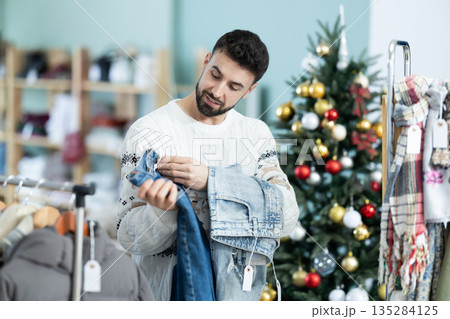 Man chooses jeans against the background of a Christmas tree in a store decorated for the holidays Man chooses jeans against the background of a Christmas tree in a store decorated for the holidays 135284125