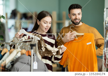 Happy elegance european couple examine and choose new clothes in modern store, woman selecting dress and man choosing t-shirt 135284174