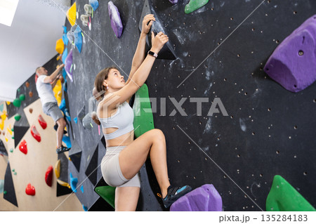 Young woman climbs steep artificial wall in sports complex and trains endurance Young woman climbs steep artificial wall in sports complex and trains endurance 135284183
