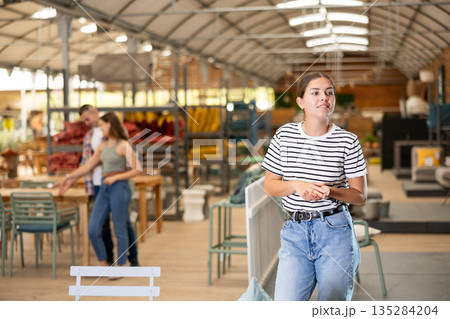 Interested girl choosing comfortable outdoor furniture at garden store 135284204