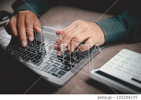 Person typing on laptop with virtual tax invoice and document icons illustrating financial data management Person typing on laptop with virtual tax invoice and document icons illustrating financial data management 135284235