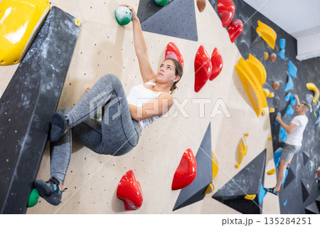 Young woman climbs steep artificial wall in sports complex and trains endurance Young woman climbs steep artificial wall in sports complex and trains endurance 135284251