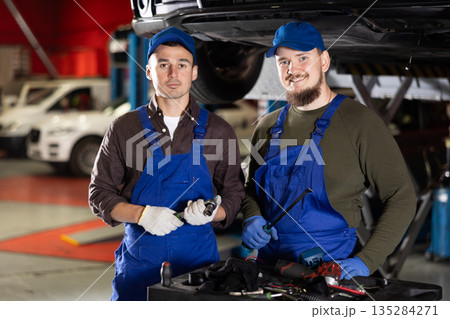 Two positive car mechanics standing in auto workshop holding repair tools 135284271