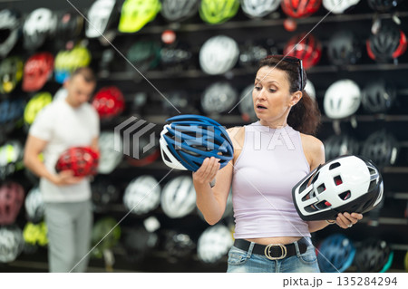 Focused woman comparing bicycle helmets in store of cycling gear 135284294