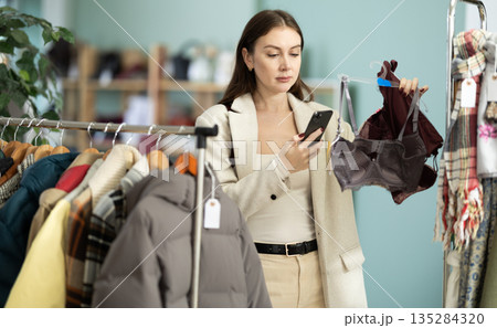 Female shopper checks quality of sexual bra by scanning QR code on label 135284320