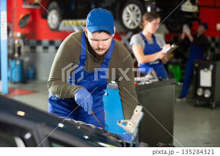 Professional mechanic man in uniform repairing car in auto repair garage Professional mechanic man in uniform repairing car in auto repair garage 135284321